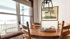 A dining area with a round wooden table surrounded by six wooden chairs, a woven placemat, and a framed picture on the wall.