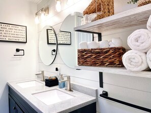 A modern bathroom with a double sink, a mirror, and a shelf with towels.