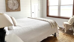 A bedroom with a bed, a chair, a door, and a window with a view.