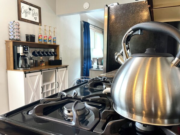 Una cocina con estufa a gas, hervidor y barra de café con diversos equipos para prepararlo.