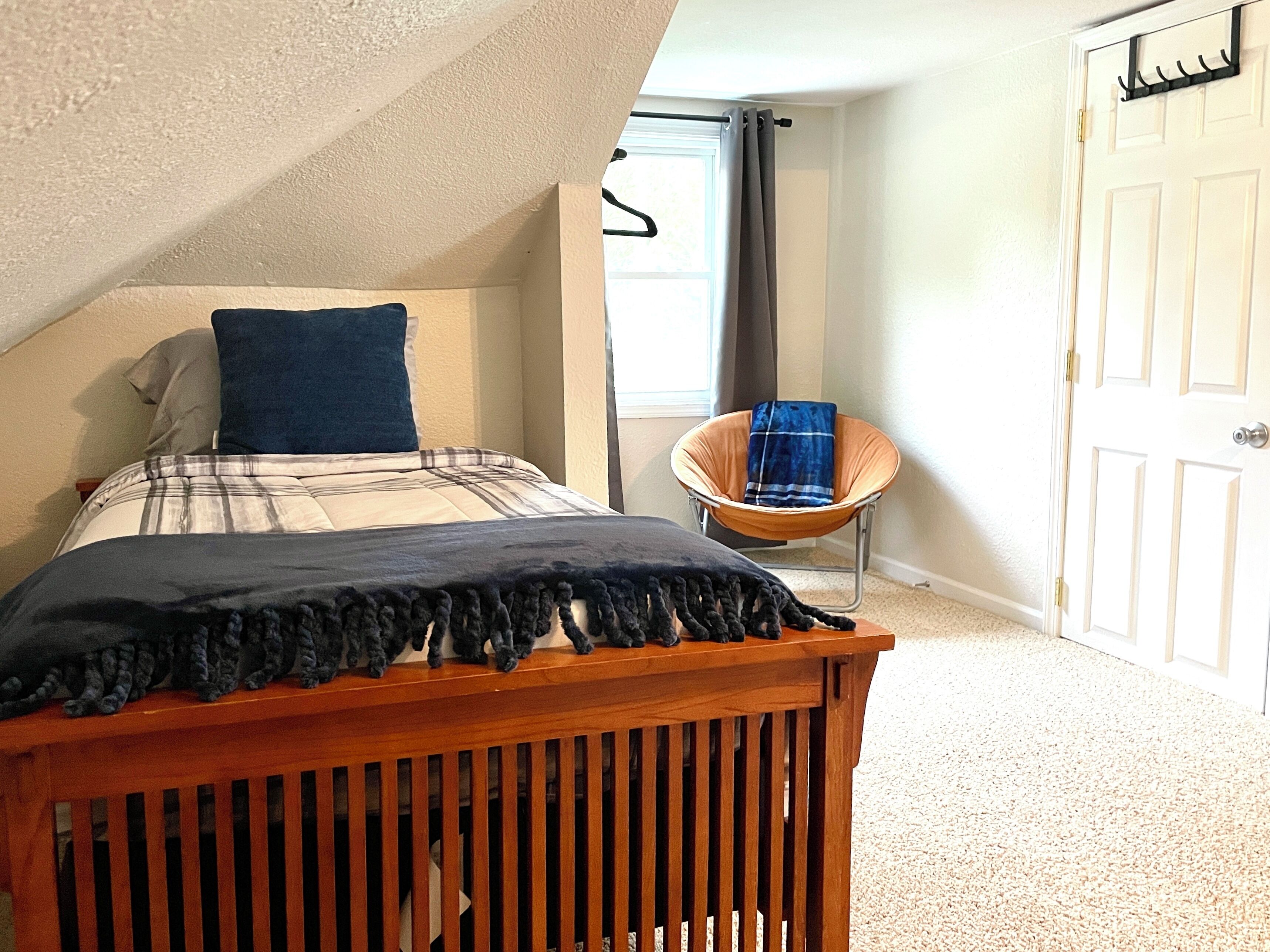 A bedroom with a bed, a chair, a door, and a window.
