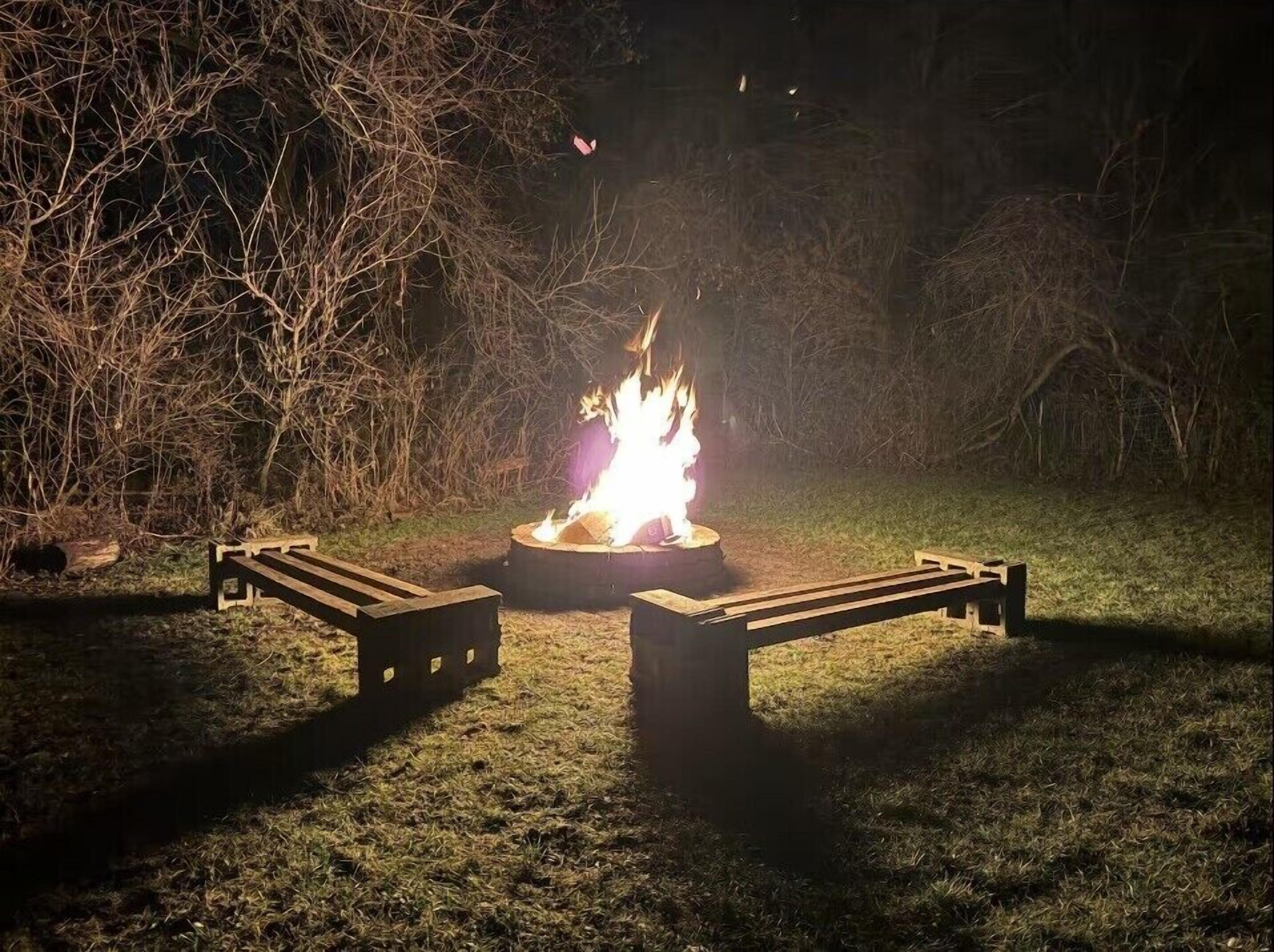 A campfire with a metal grill in a grassy area surrounded by trees.