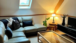 Ett mysigt vardagsrum med en hörnsoffa, ett soffbord i glas, ett piano och ett takfönster.
