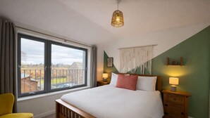 Ein Schlafzimmer mit einem großen Bett, einem Fenster mit Blick auf die Landschaft, einem gelben Sessel und einer Hängelampe.