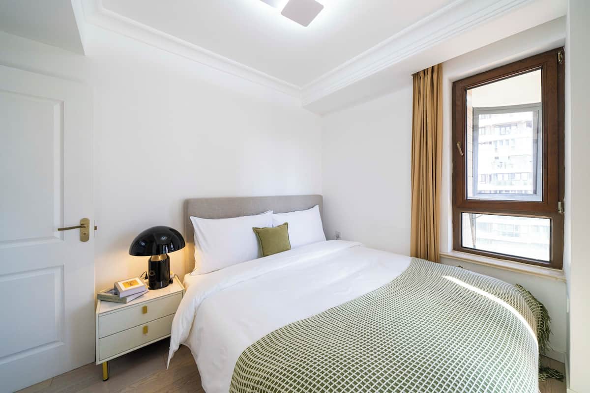 Une chambre d’hôtel avec un lit, une table de chevet, une lampe, une fenêtre avec des rideaux et une porte.