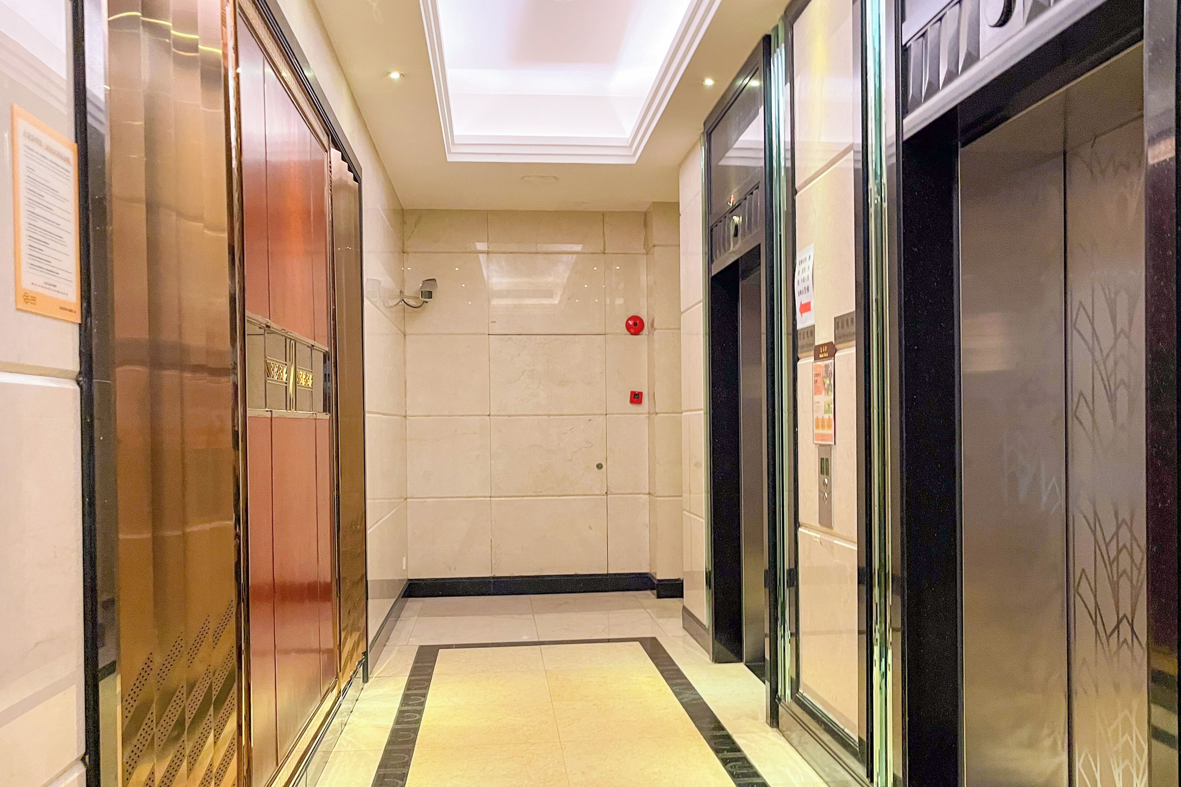 A modern elevator area with a tiled floor, glass doors, and a ceiling light.