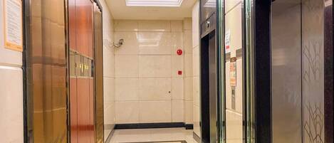 A modern elevator area with a tiled floor, glass doors, and a ceiling light.