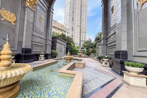 Un patio con una fuente, suelo de baldosas y un edificio alto al fondo.