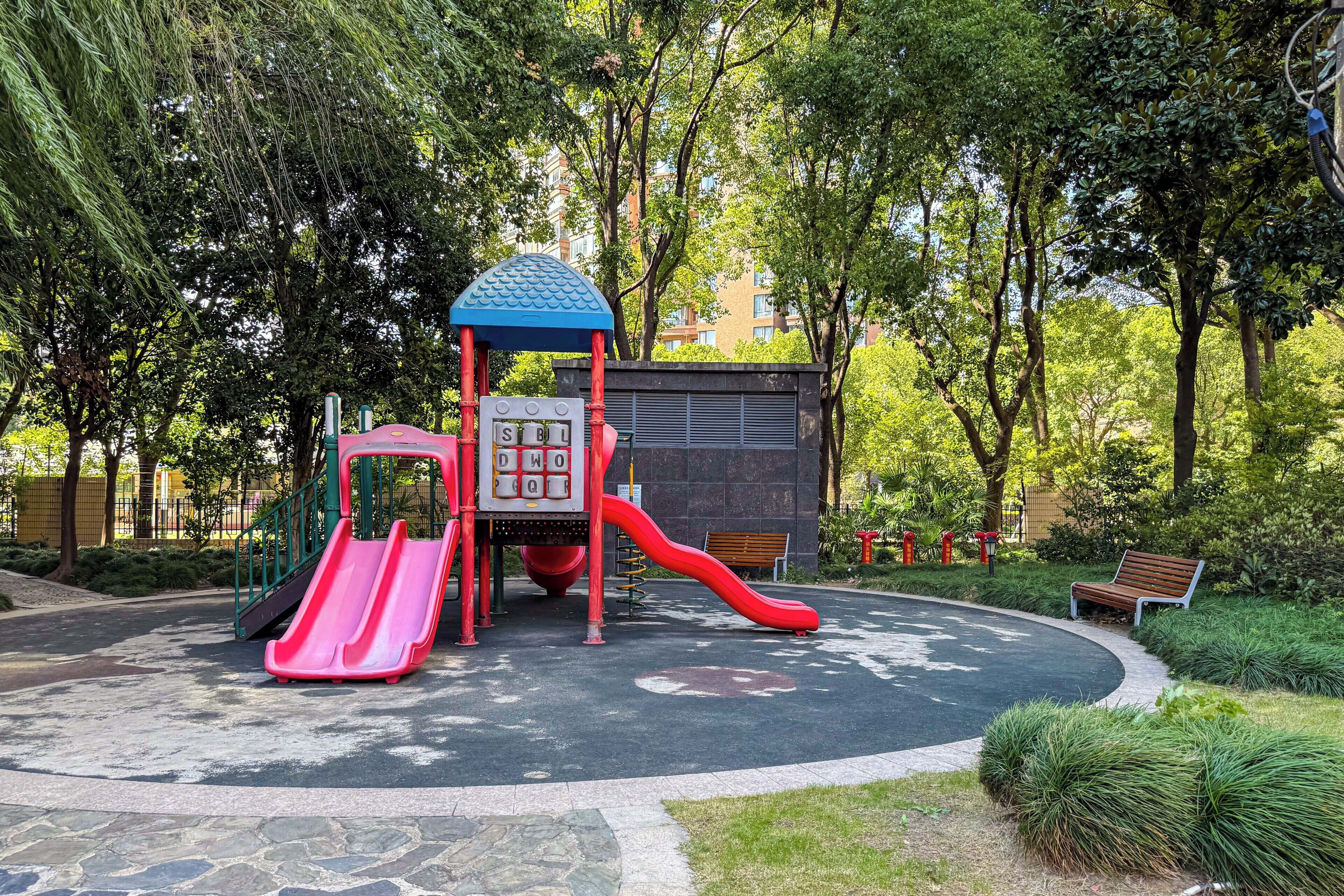 Un parque infantil con toboganes y estructuras de juego, rodeado de árboles y bancos.