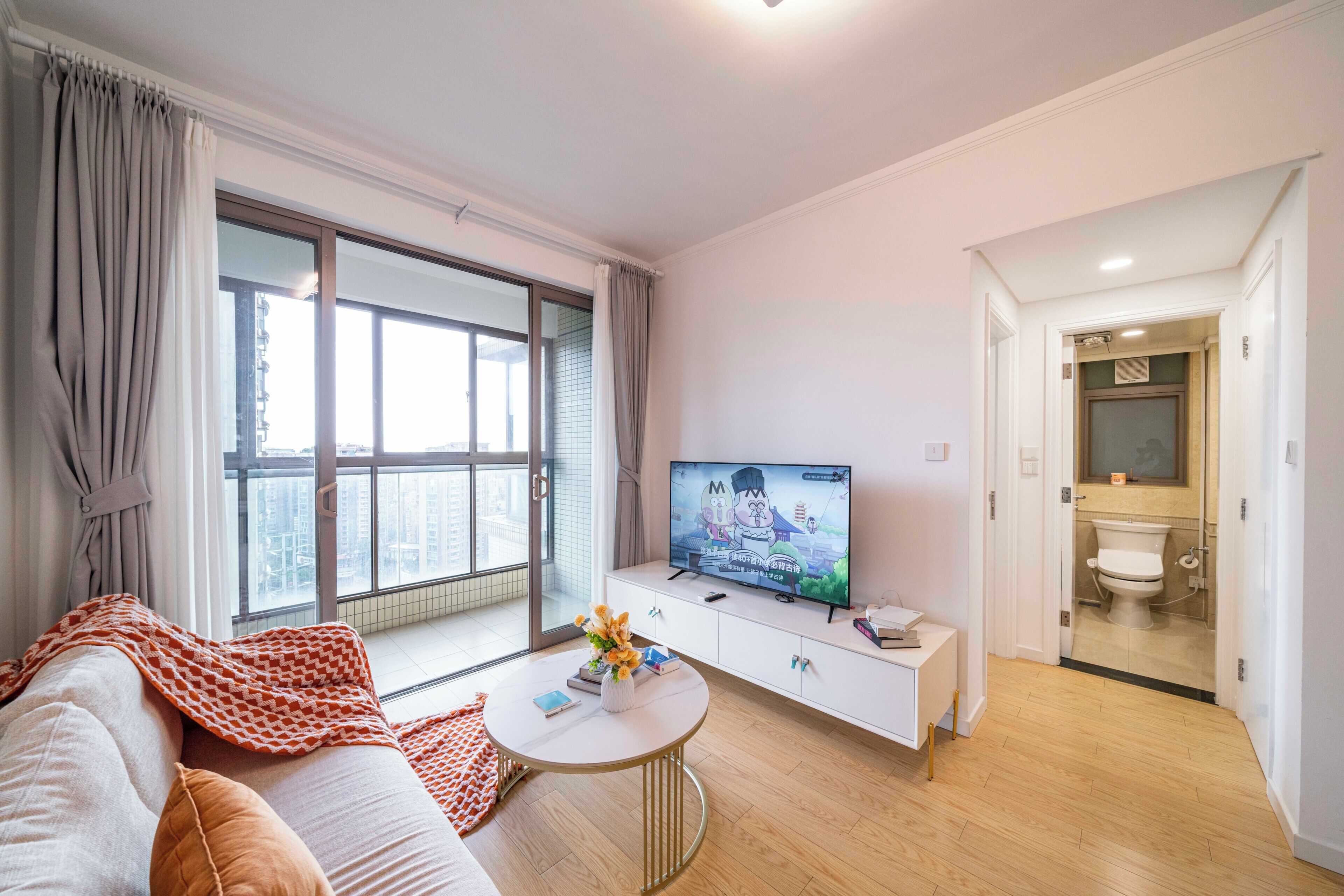 Un salon moderne avec un canapé, une table basse, un téléviseur et une vue sur la ville grâce à une grande fenêtre.