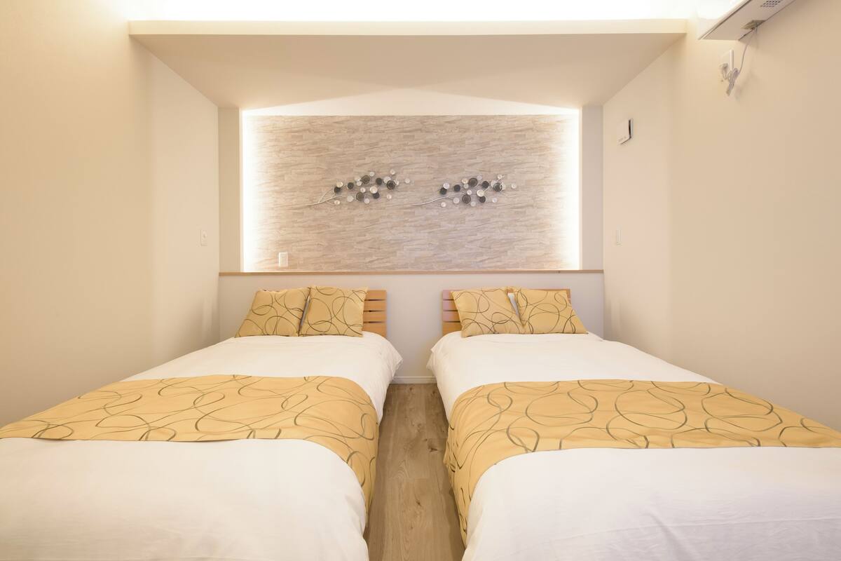 Une chambre d’hôtel avec deux lits, une fenêtre avec un luminaire et une œuvre d’art accrochée au mur.