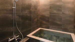 Een moderne badkamer met een vrijstaand bad, een handdouche en een bedieningspaneel aan de muur.