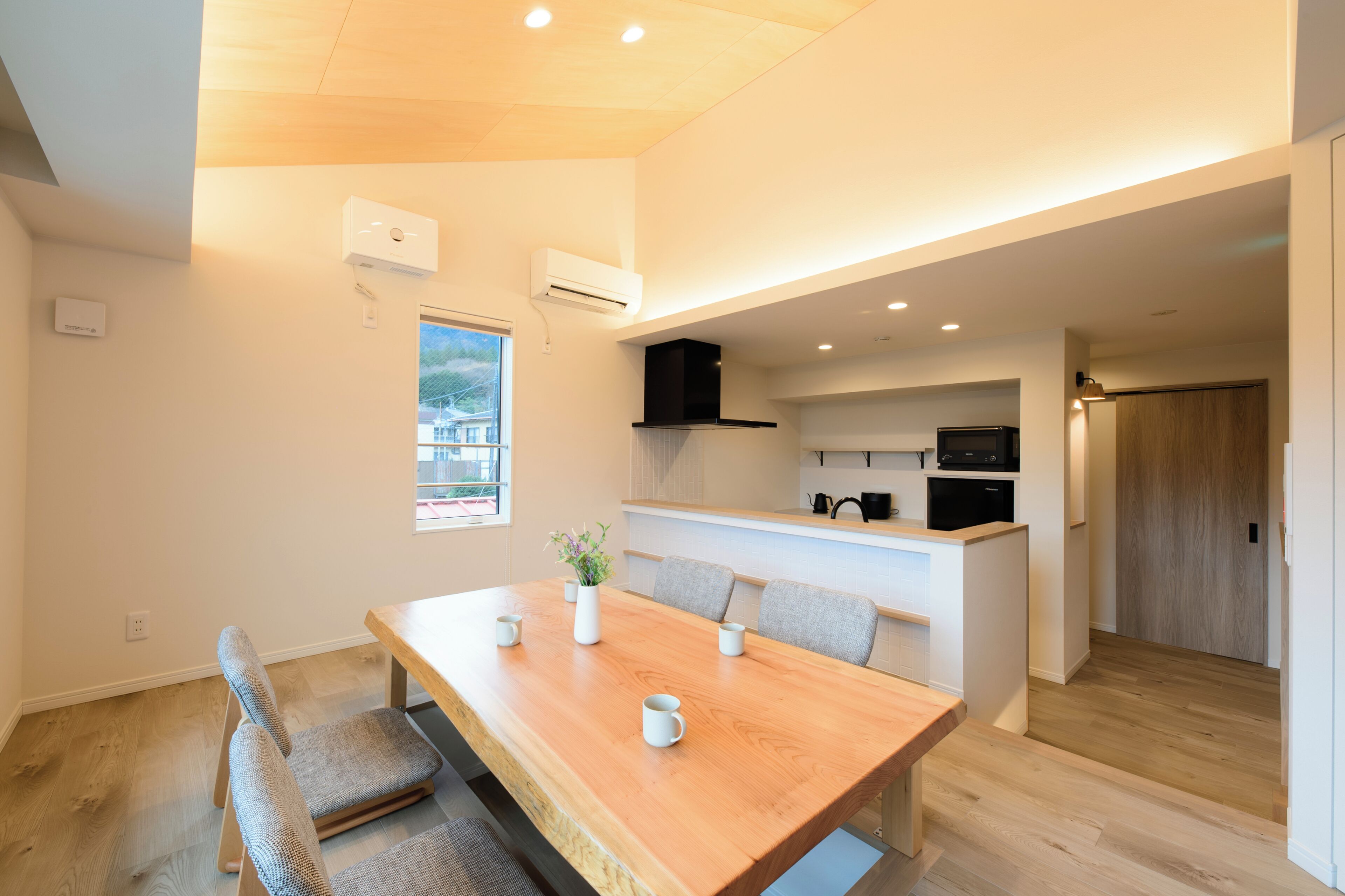 Una cocina moderna con una mesa de comedor de madera, sillas grises y una pequeña isla con microondas y tostadora.