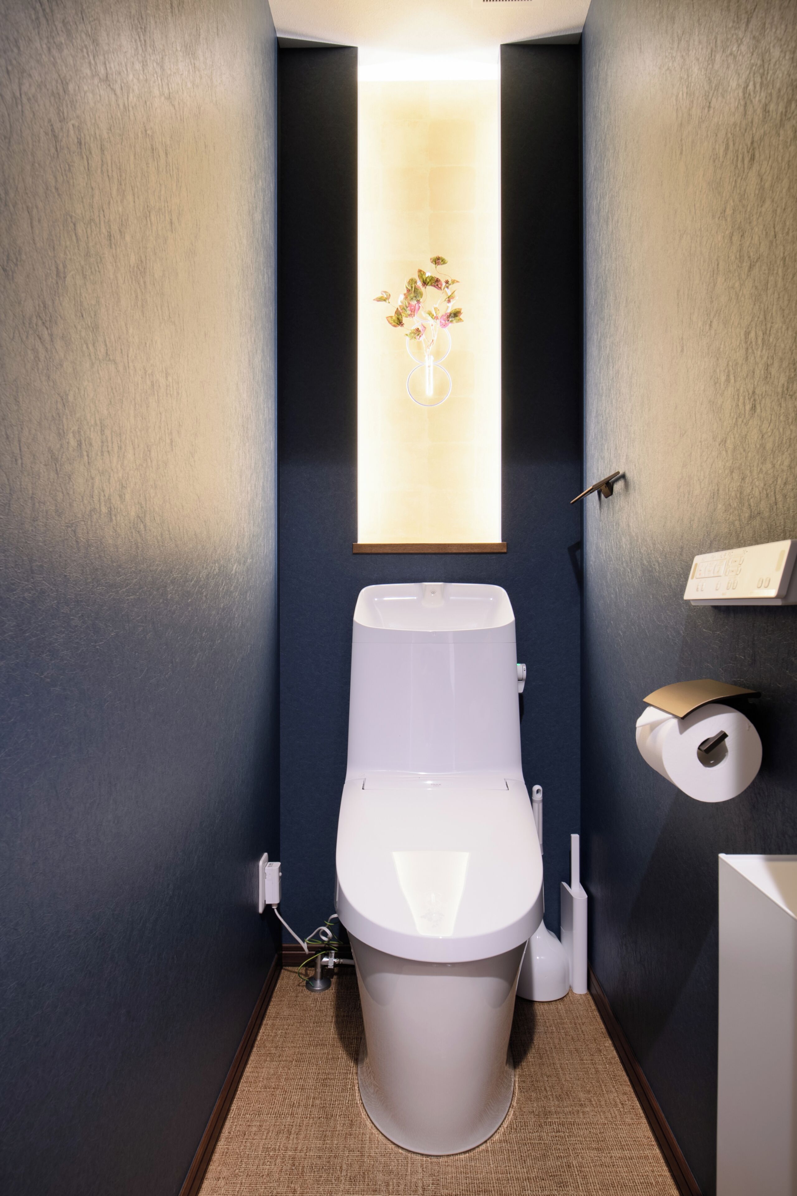 Un baño moderno con un inodoro blanco, un dispensador de papel higiénico montado en la pared y un cuadro con flores.