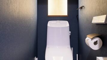 Un baño moderno con un inodoro blanco, un dispensador de papel higiénico montado en la pared y un cuadro con flores.