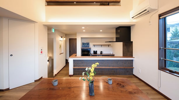 Een moderne keuken met een houten kookeiland, een eethoek met een houten tafel, en uitzicht op buiten door een groot raam.