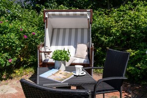 Eine Gartenpatio mit Liegestuhl im Streifenmuster, einem kleinen Tisch mit einem Buch und einer Tasse, sowie einem Blumentopf.