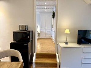 Eine moderne Küche mit Mikrowelle, Toaster und Herd, ein Essbereich mit einem Stuhl, ein Fernseher auf einem Standfuß und eine Treppe, die zu einem Flur führt.