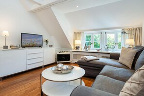 Ein modernes Wohnzimmer mit Sofa, Fernseher, Couchtisch und einem Essbereich mit Tisch und Stühlen.