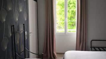 Een slaapkamer met een bed, een stoel, een bureau en een raam met gordijnen.