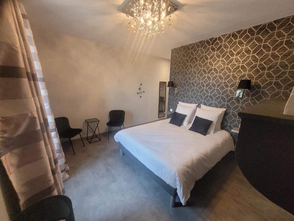 A bedroom with a large bed, a small desk, a chair, and a patterned wall.