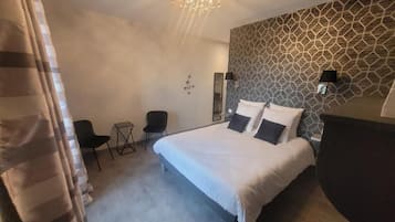 A bedroom with a large bed, a small desk, a chair, and a patterned wall.