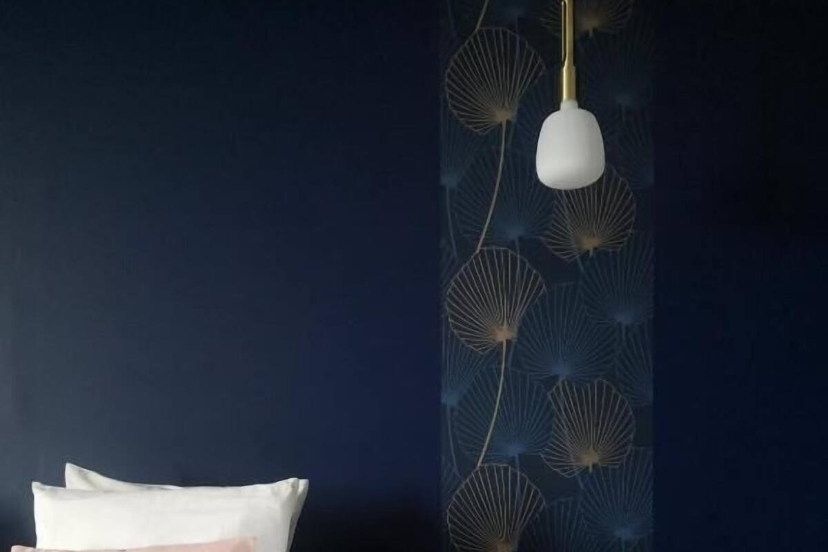 A bedroom with a bed, pillows, a nightstand, and a wall with a decorative pattern.