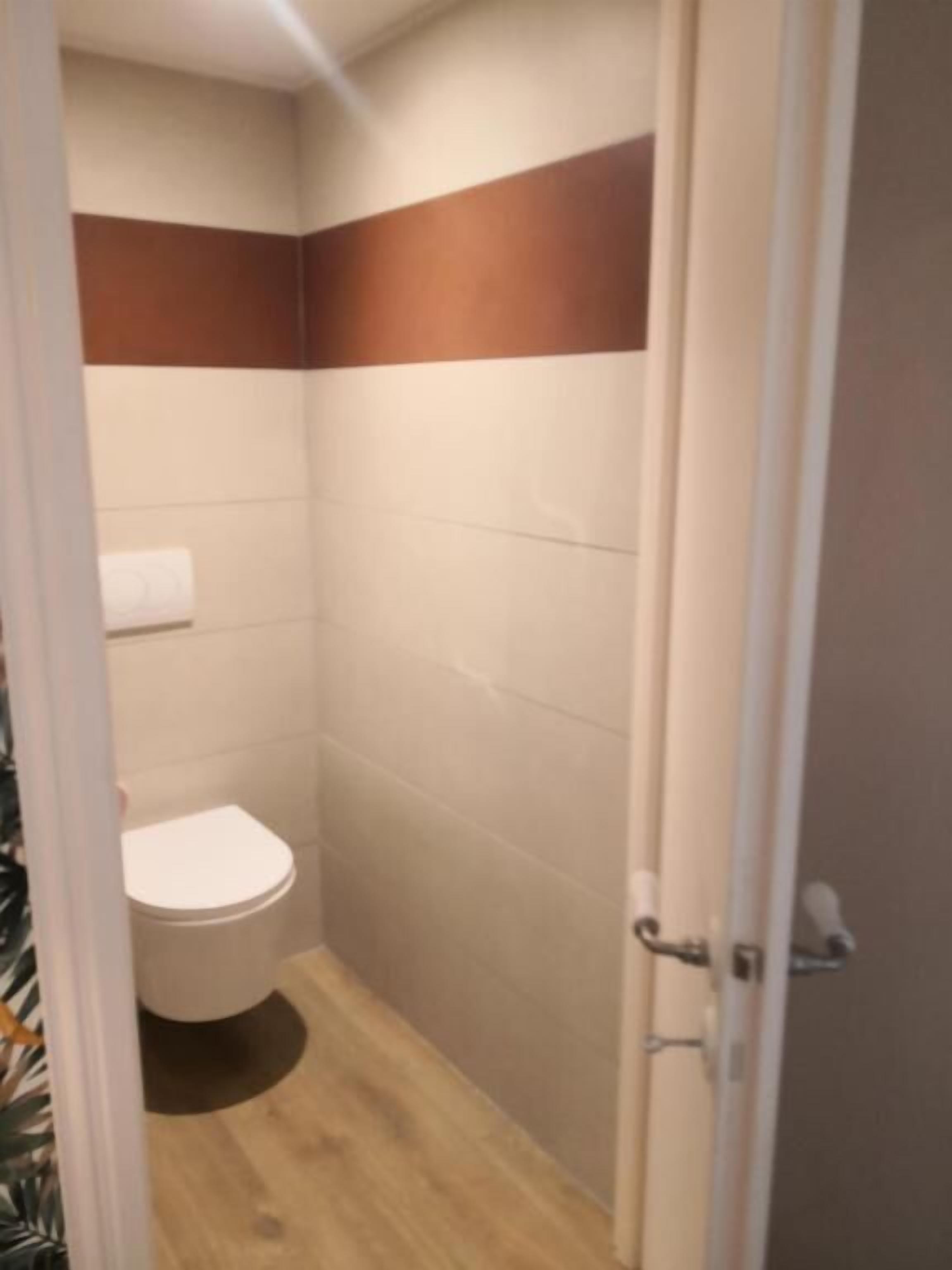 Ein kleines, schmales Badezimmer mit Toilette, Handtuchspender und Duschbereich.