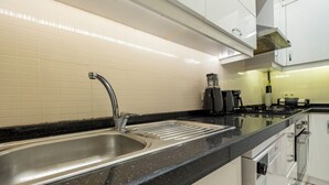 A modern kitchen with a stainless steel sink, black countertop, white cabinets, and a coffee maker. - Spacious 3-Bedroom, 2-Bathroom Family Apartment in Central Location No Stair (İstanbul)