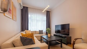 A modern living room with a sofa, a coffee table, a TV, and a plant. - Spacious 3-Bedroom, 2-Bathroom Family Apartment in Central Location No Stair (İstanbul)