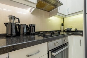 A modern kitchen with a black countertop, white cabinets, a gas stove, and a coffee maker. - Spacious 3-Bedroom, 2-Bathroom Family Apartment in Central Location No Stair (İstanbul)