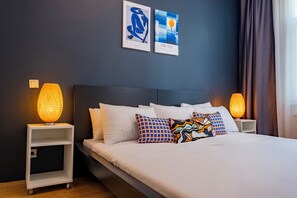 A modern hotel room with a large bed, white bedding, and colorful pillows. There are two wall-mounted artworks and a standing lamp on either side of the bed. - Spacious 3-Bedroom, 2-Bathroom Family Apartment in Central Location No Stair (İstanbul)