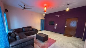 Ein Wohnzimmer mit einem Ecksofa, einem Couchtisch, einem Deckenventilator und einem an der Wand montierten Fernseher.