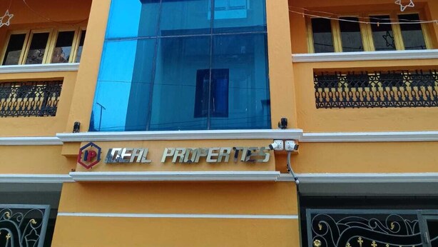 Ein mehrstöckiges Gebäude mit einer auffälligen, blauen Glasfassade, einem Schild mit der Aufschrift "TEAM PROPERTIES" und Balkonen mit dekorativen Geländern.