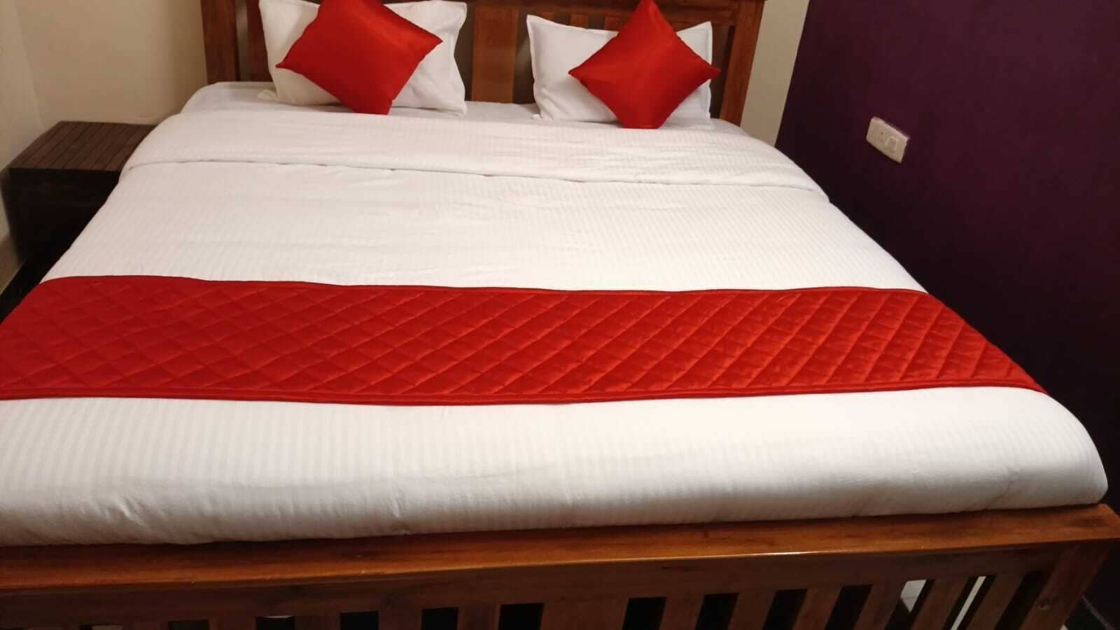 Una cama con una colcha blanca y roja, dos almohadas rojas y un cabecero de madera.
