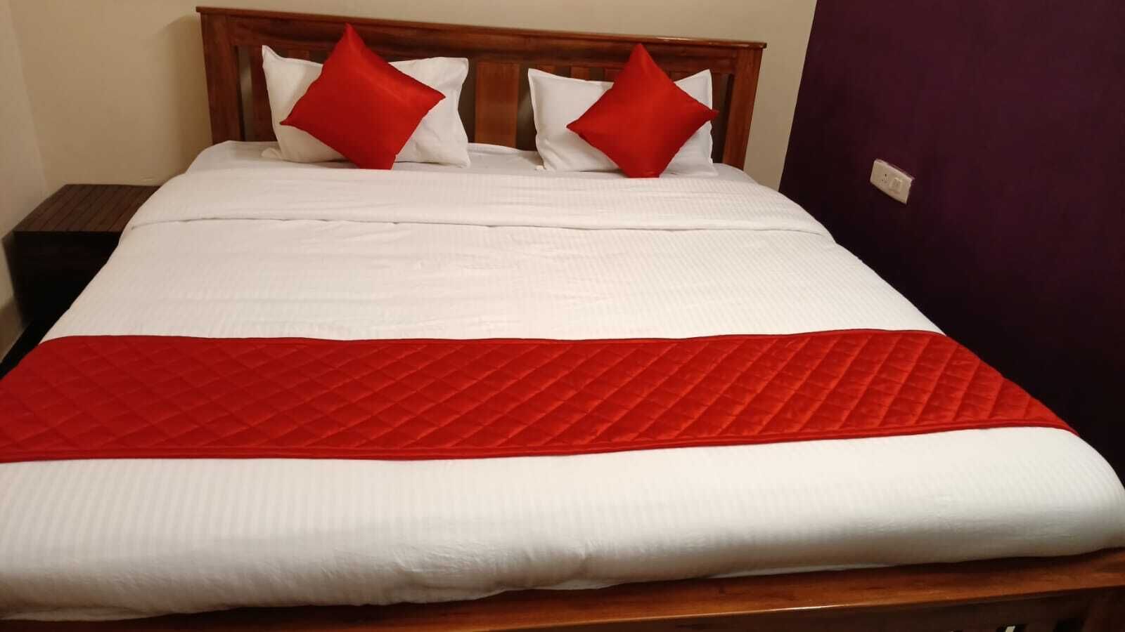 Una cama bien hecha con ropa blanca y una colcha acolchada roja, dos almohadas rojas y un cabecero de madera.