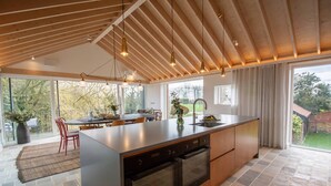 Een moderne keuken met een groot eiland, houten balken in het plafond en een eethoek met uitzicht op de tuin.