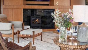 Een gezellige woonkamer met een open haard, houten meubels en een aan de muur bevestigde televisie.