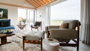 Een ruime woonkamer met een groot raam, een blauwe bank, een houten stoel en een beige fauteuil.