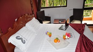 Un lit bien fait, avec un ordinateur portable, deux boissons et des fruits disposés sur un plateau.