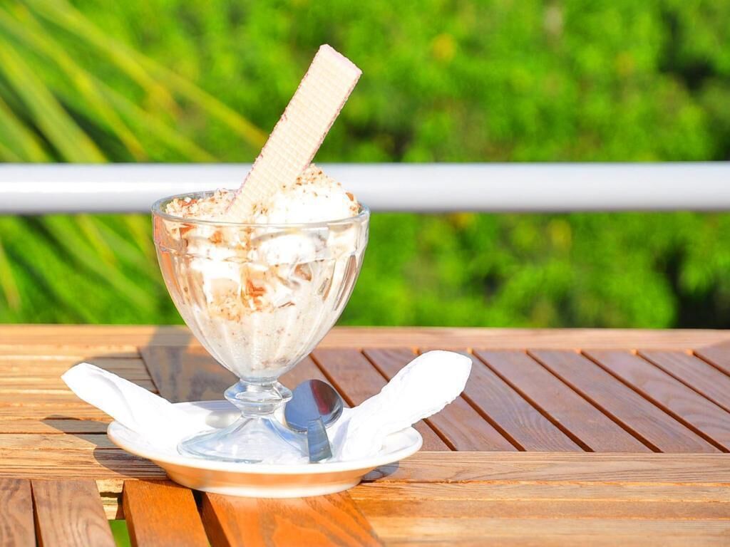 Een dessert op een houten tafel met een witte servet en lepel, buiten met groen in de achtergrond.