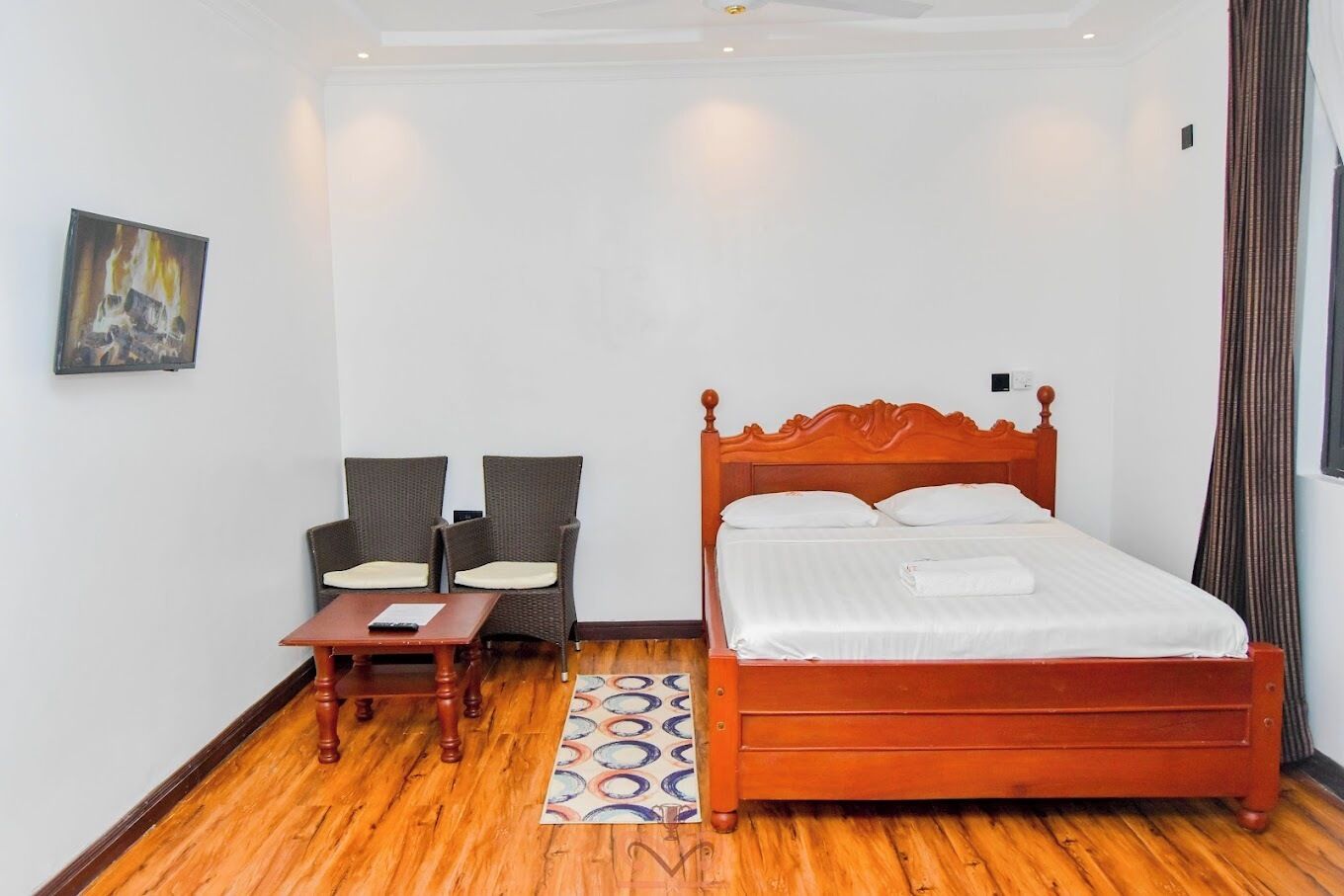 Ein Hotelzimmer mit einem hölzernen Bett, zwei Stühlen, einem kleinen Tisch und einem Gemälde an der Wand.