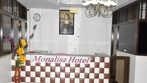 Un comptoir d’accueil à l’hôtel Monalisa, orné d’un motif à carreaux, avec une horloge et une œuvre d’art encadrée au-dessus.