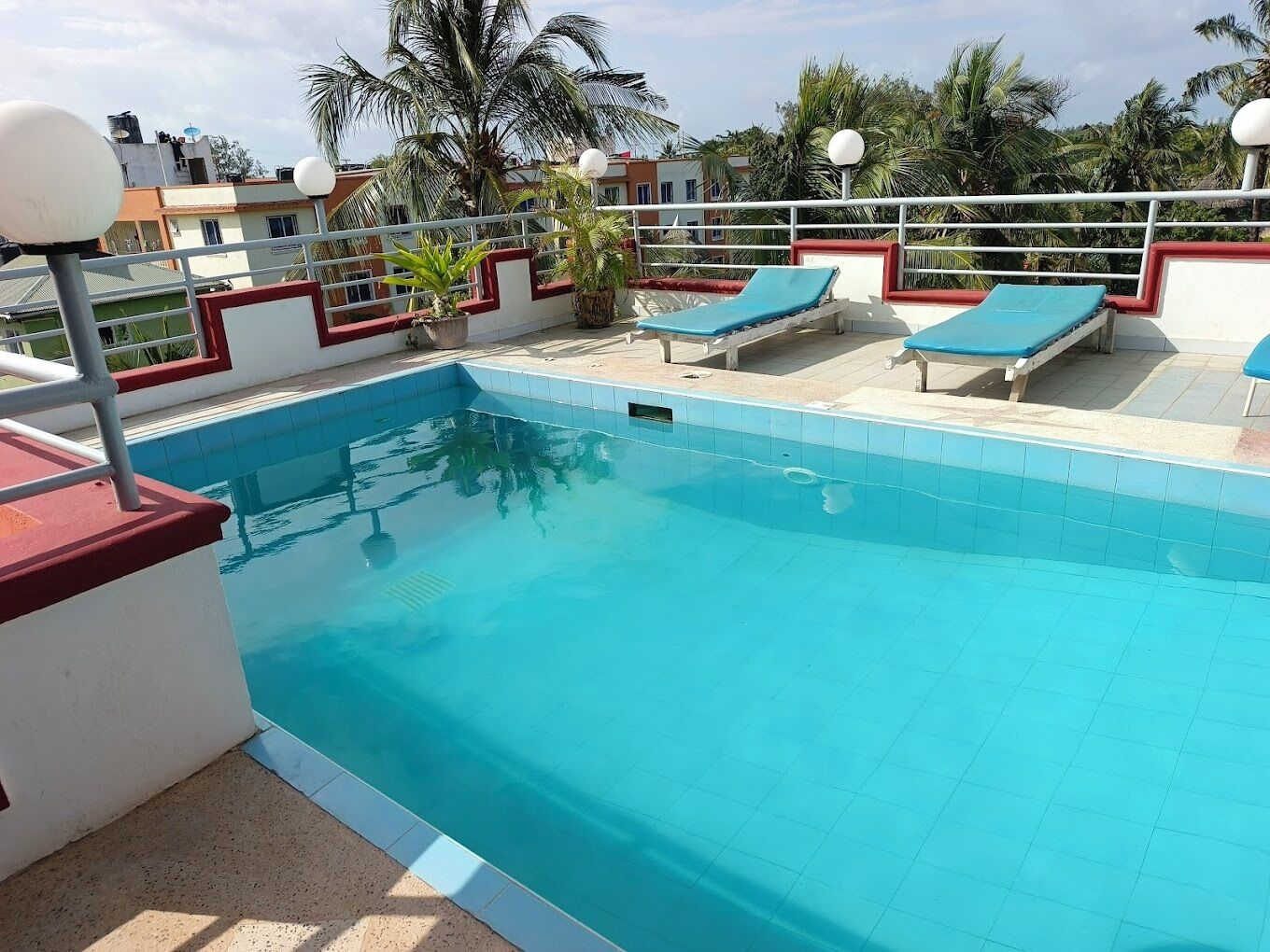 Ein Dachpool mit blauen Fliesen, einer roten und weißen Geländer und mehreren Liegestühlen.