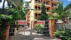 Un hôtel à plusieurs étages, doté d’une entrée sécurisée par un portail, entouré de verdure et de palmiers.