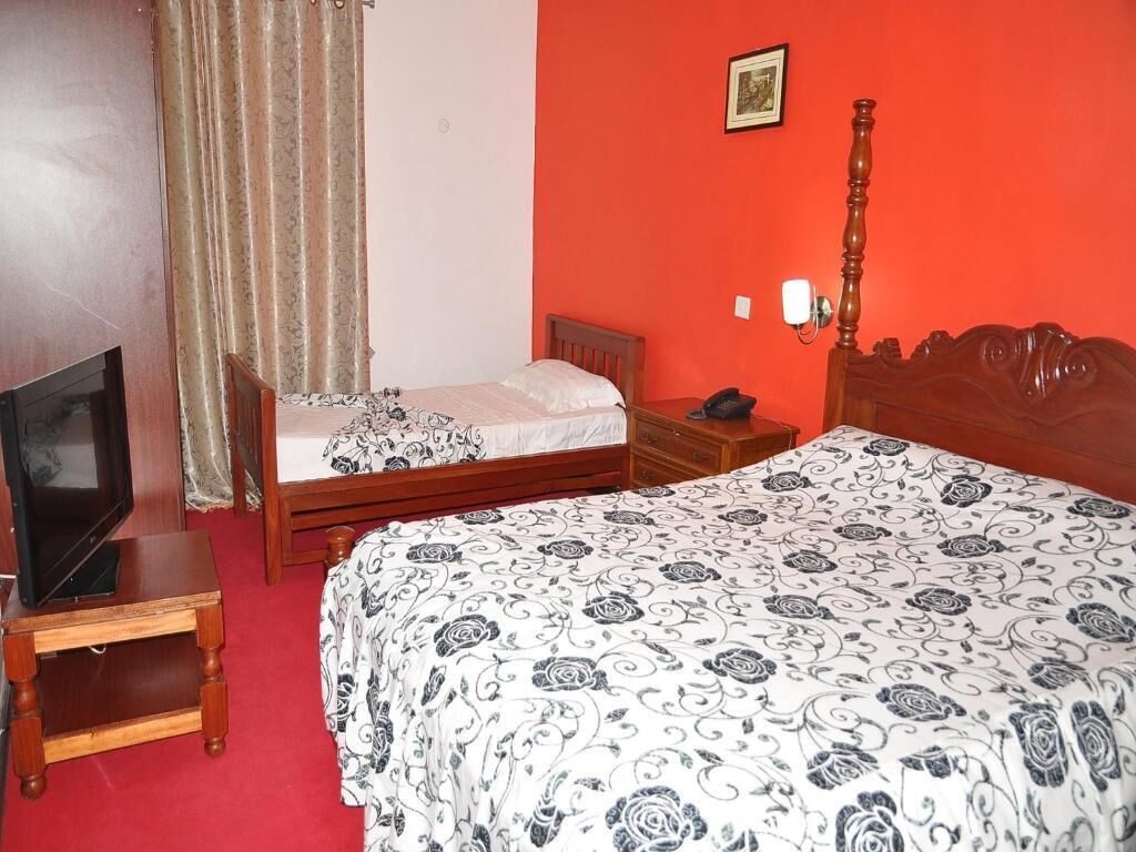 A room with two beds, a TV on a small table, and a red wall.