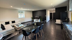 Ein modernes Wohnzimmer mit einer Couch, einem Esstisch mit Stühlen, einem Fernseher und einer Küchenzeile mit Herd.