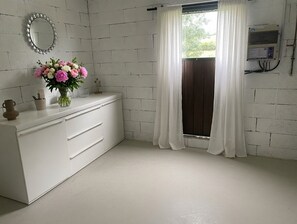 Une salle de bain avec un meuble-lavabo blanc, un miroir, un vase de fleurs et une fenêtre avec des rideaux.