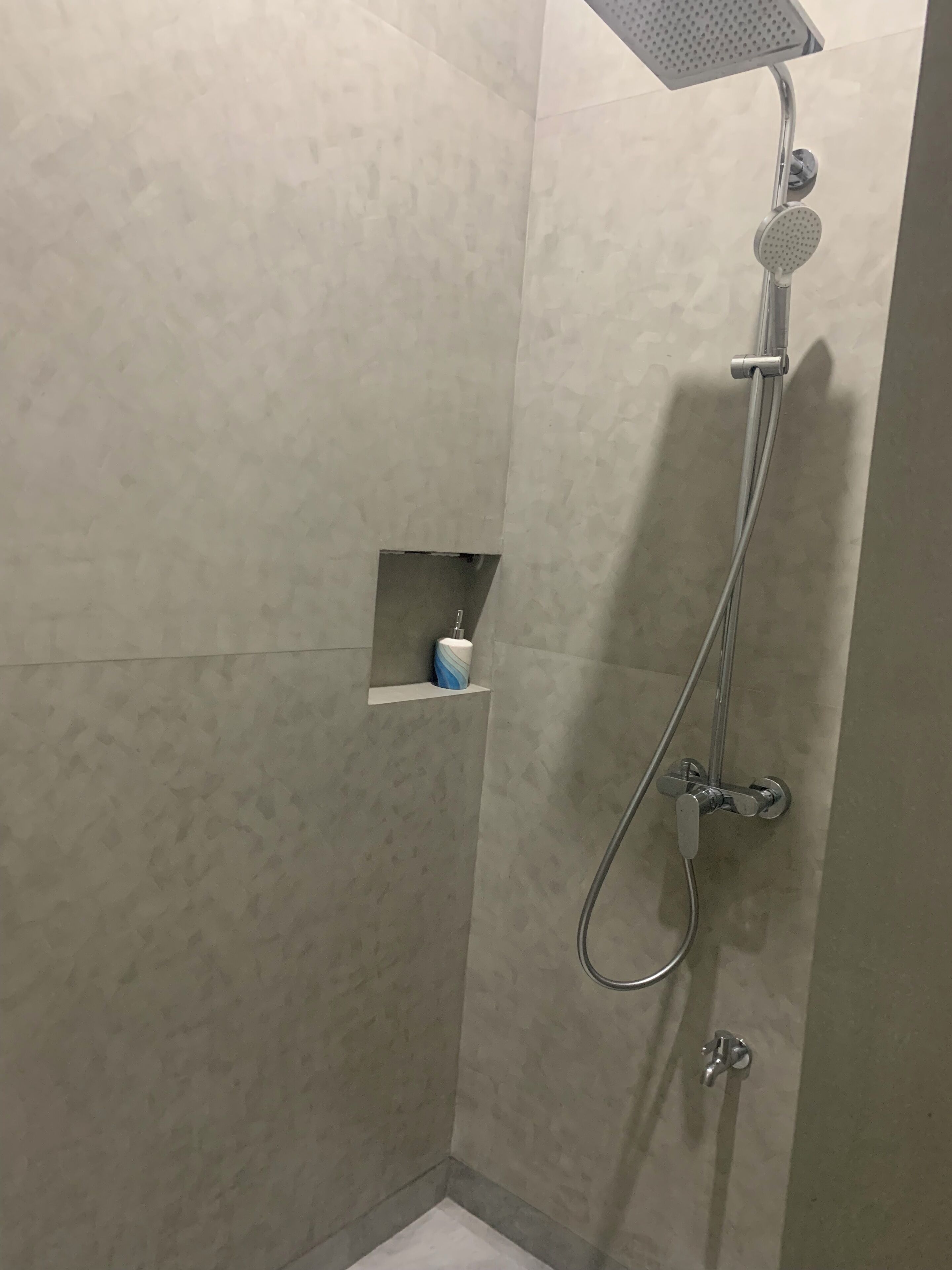 Ein Duschbereich mit Handbrause, Wandarmatur und einer kleinen Ablage mit Toilettenpapier.