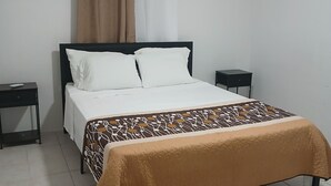 Een slaapkamer met een bed, twee nachtkastjes, een raam met gordijnen en een betegelde vloer.